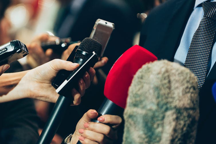 A group of journalists holding microphones during a media scrum.