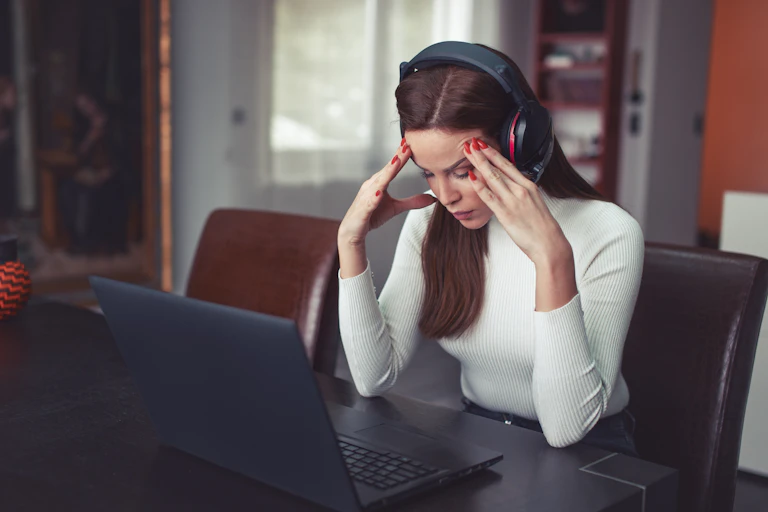A woman wearing headphones with her hands on her temple