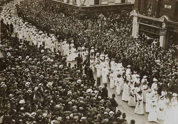 A stream of women in white between crowds of men in black.