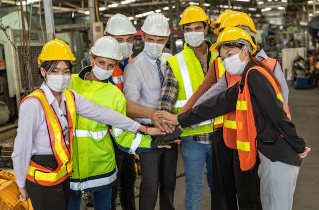 Masked workers in hard hats touch hands