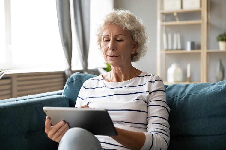 A senior woman uses an iPad on the couch.