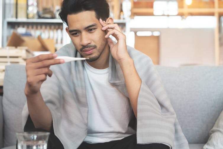 A young man looks at a thermometer.