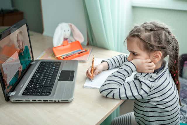 Primary school girl watching teacher on computer at home