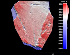 A scale bar in blue and red is visible to the right of a smooth piece of stone, also in blue and red, that features a triangular shape.