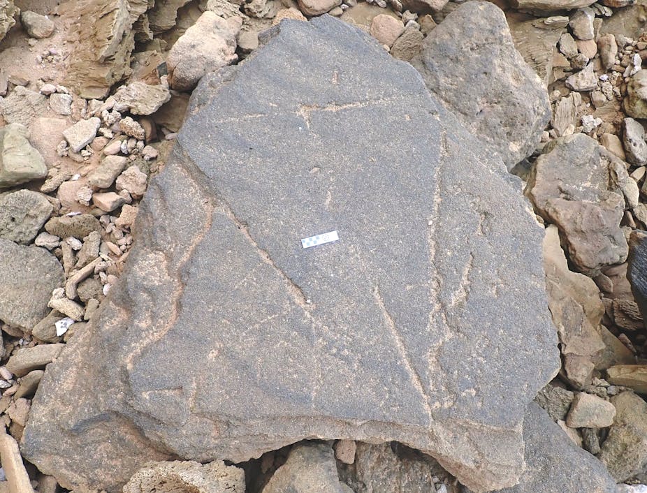 A large stone lies in a pile of smaller stones. A three-sided shape is visibly etched into its surface.