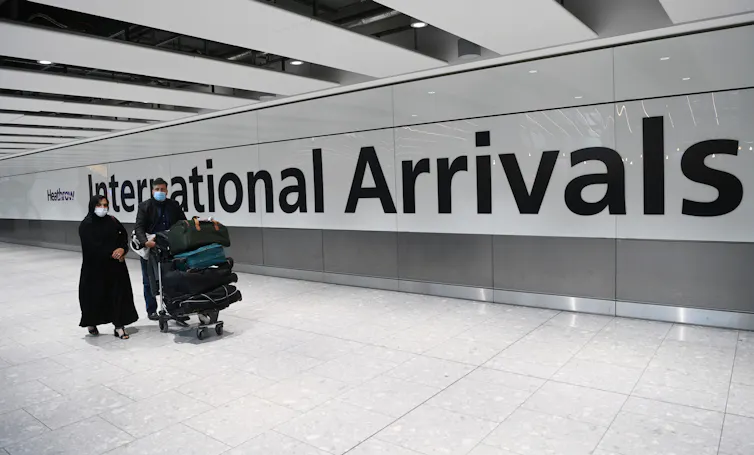 Two people walking into the arrivals terminal with luggage at Heathrow