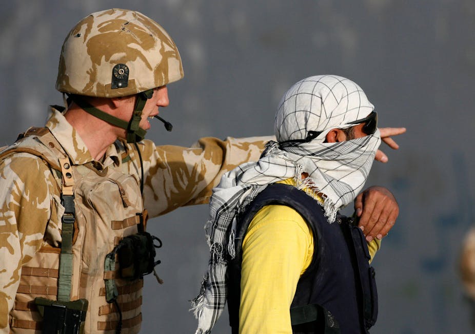 A man wearing British military uniform speaks to an Afghani man wearing sunglasses and a headscarf.