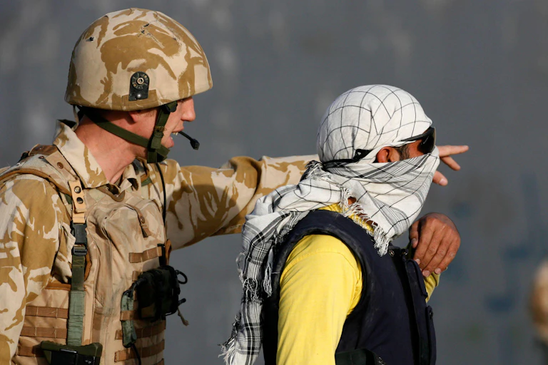 A man wearing British military uniform speaks to an Afghani man wearing sunglasses and a headscarf.
