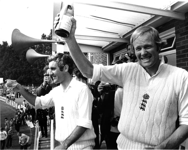 Black and White picture of two men in cricket gear with a trophy.