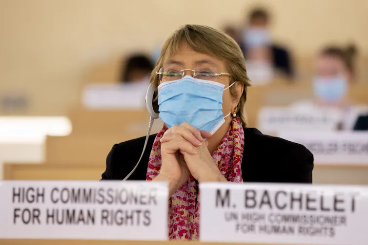 Woman wearing headphones and face mask sits listening.