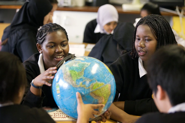 Two black schoolgirls with braids sit in front of two other schoolgirls wearing hijabs