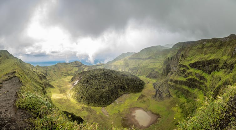 The La Soufriere volcano crater, covered in green, with clouds in the background.