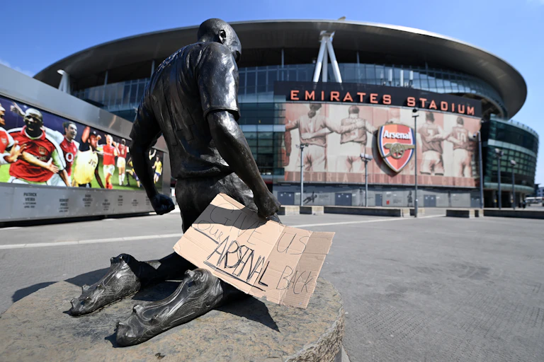 Statue outside of Arsenal Emirates Stadiium with sign saying "Give us our Arsenal Back"