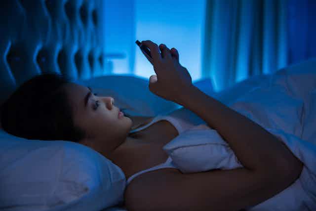 A woman lies in bed holding a mobile phone.