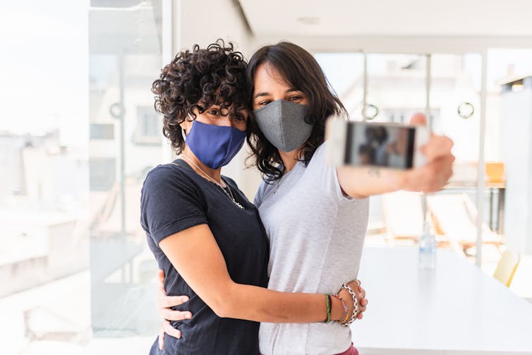Two women wearing face masks pose for a selfie