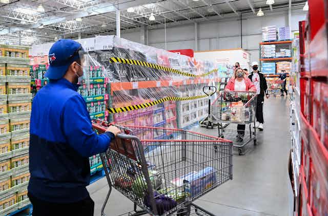 People wearing masks push their shopping carts in a Costco.