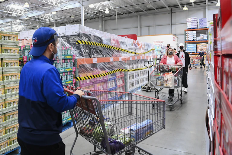 People wearing masks push their shopping carts in a Costco.