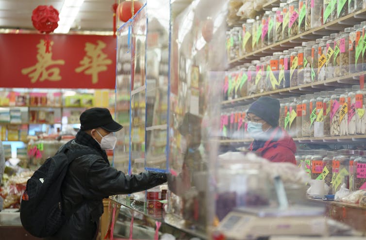 A man wearing a mask shops at a store in Chinatown in Vancouver. The cashier is behind a plastic sheet.