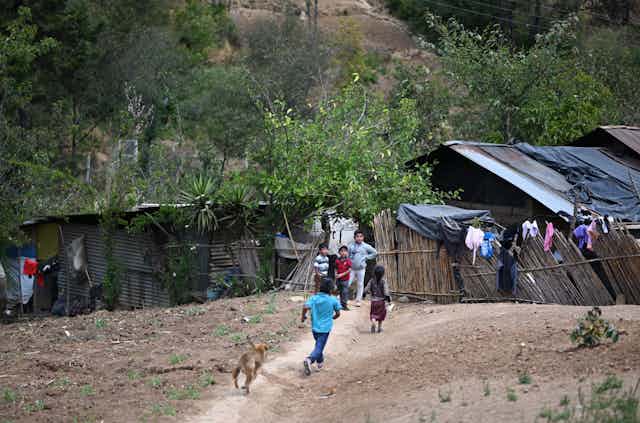 Children play with a dog in a dusty area with shacks in the background