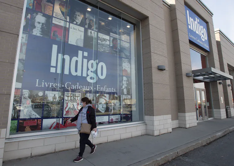 A woman in a mask walks by an Indigo store.