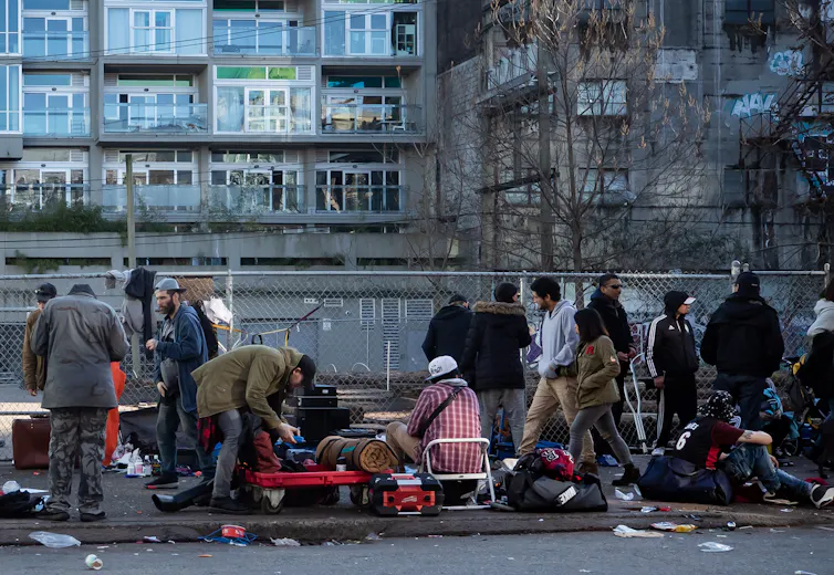 A number of people, including homeless people, gather on a crowded street in Vancouver.