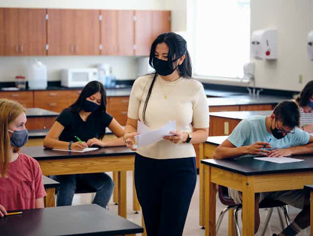 A high school teacher and students both wear masks in a classroom.
