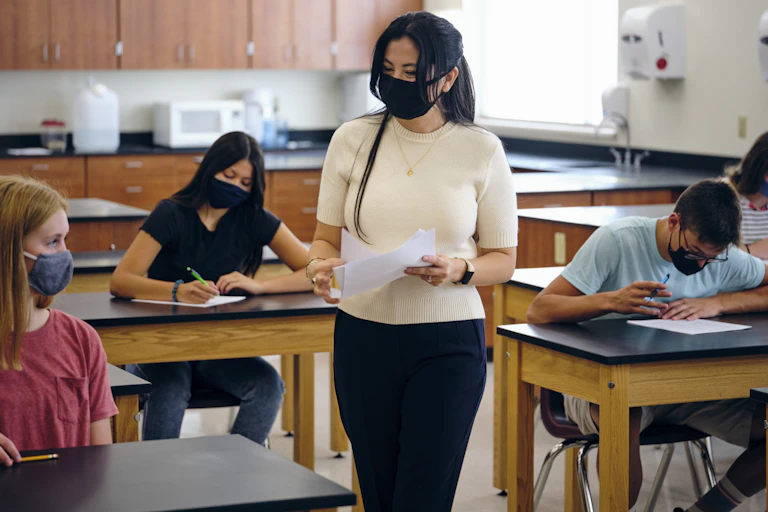 A high school teacher and students both wear masks in a classroom.