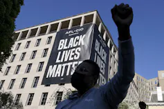 A man raises his fist in front of a Black Lives Matter banner.