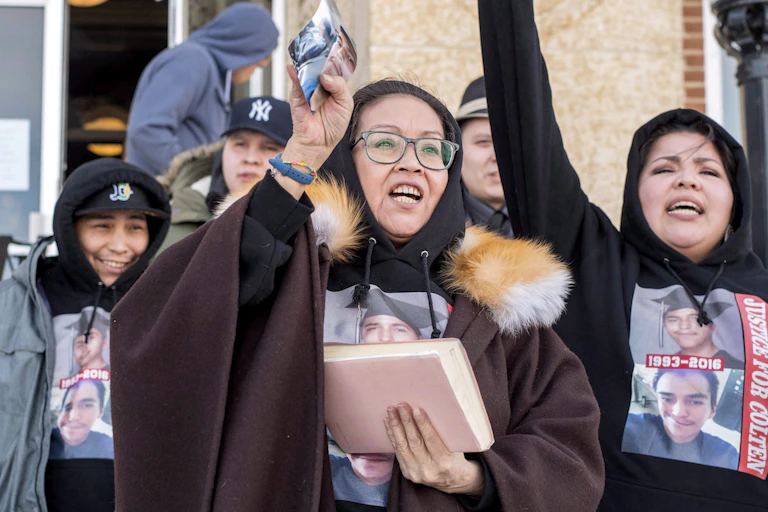 A woman holds up a photo of her son. Next to her family raise their arms.