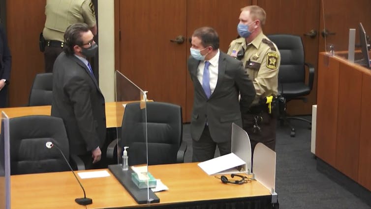 A sheriff's deputy handcuffs Derek Chauvin in the courtroom, while Chauvin speaks to his attorney