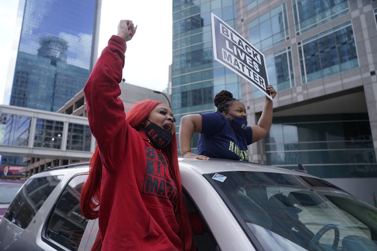 Black women cheer, one carrying a Black Lives Matter sign.