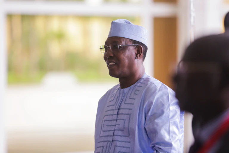 Man in cap and West African style tunic, smiling, with spectacles