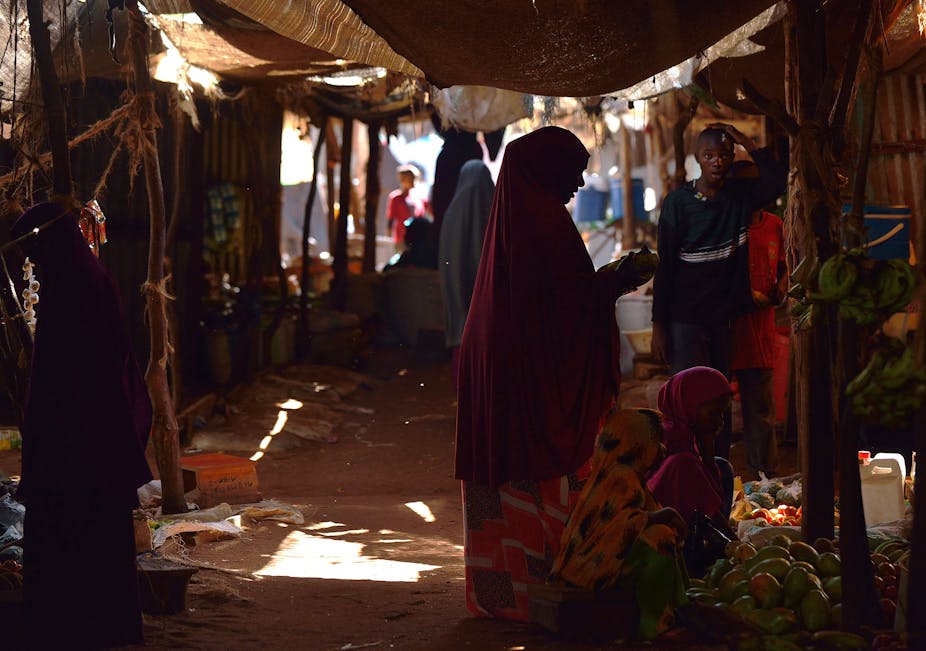 A woman in a flowing red cover-all shops for fruits and vegetables at a market
