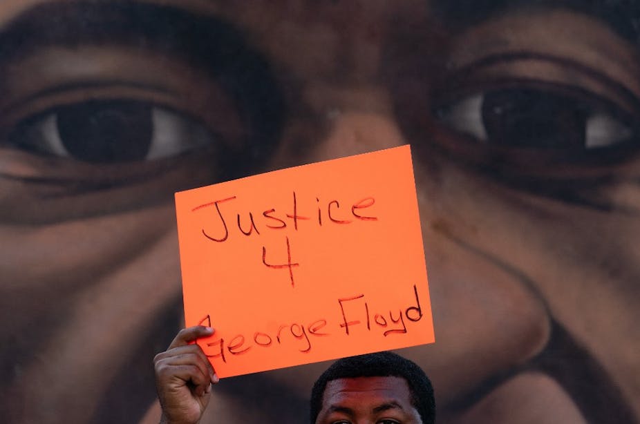 Un homme brandit une pancarte devant une fresque représentant George Floyd après l'annonce de la la reconnaissance de la culpabilité de Derek Chauvin, le 20 avril 2021, à Atlanta