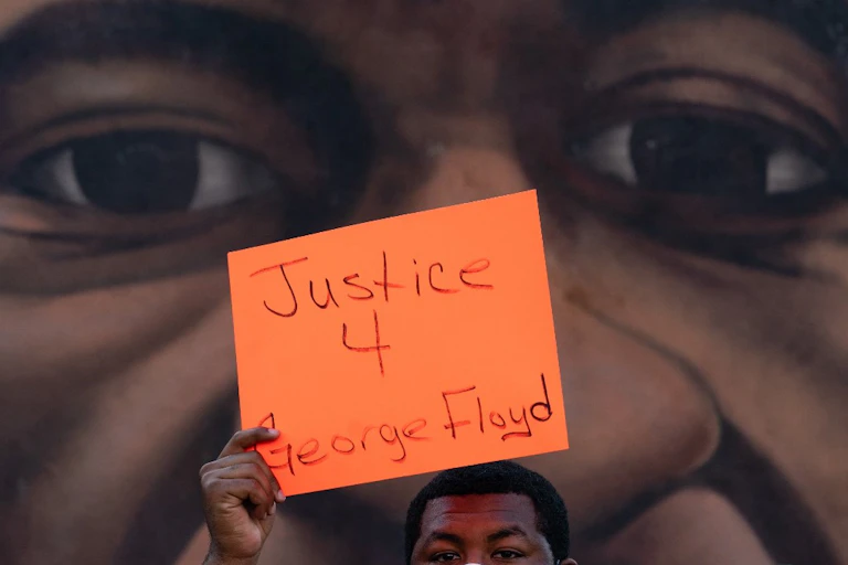 Un homme brandit une pancarte devant une fresque représentant George Floyd après l'annonce de la la reconnaissance de la culpabilité de Derek Chauvin, le 20 avril 2021, à Atlanta