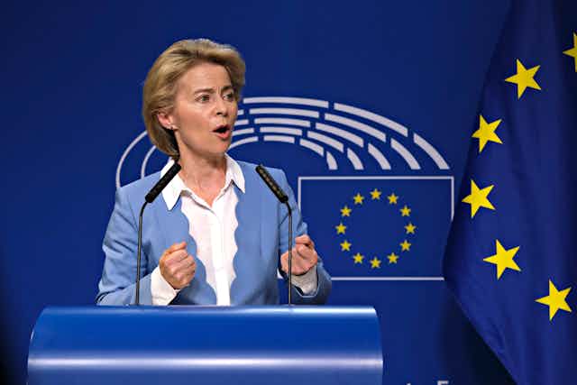 Ursula von der Leyen speaking in front of an EU flag