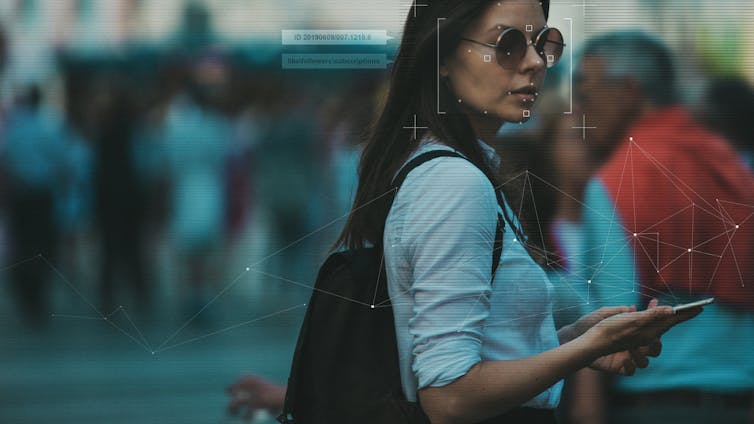 A woman holding a phone has facial recognition graphics around her face