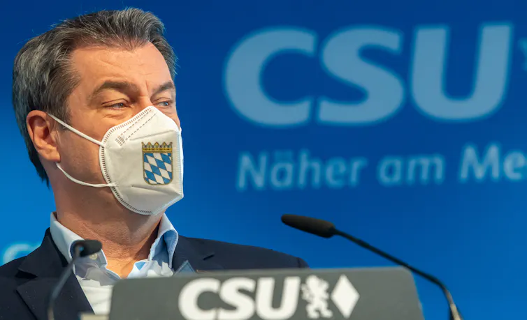 Bavarian State Premier Markus Soeder attends a press conference wearing a facemask decorated with the Bavarian coat of arms.