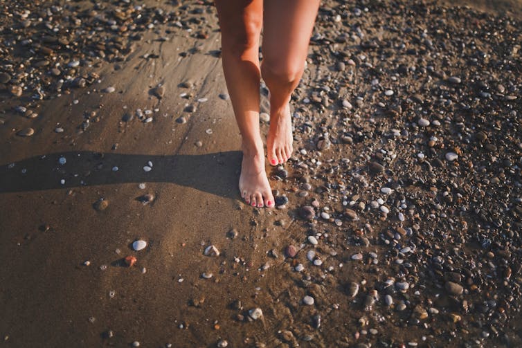 Person walking barefoot on a pebble beach.