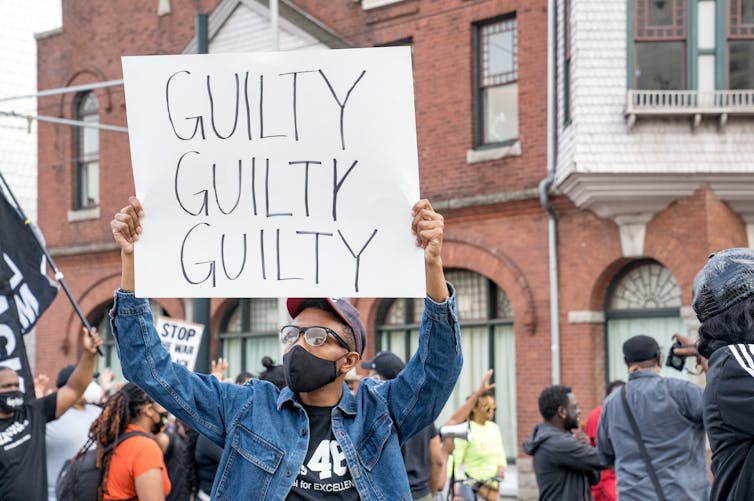 person holding sign reading guilty guilty guilty