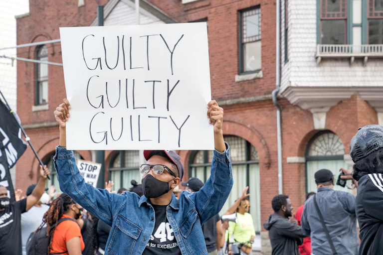 A person in a crowd holding a sign that says, "GUILTY GUILTY GUILTY"