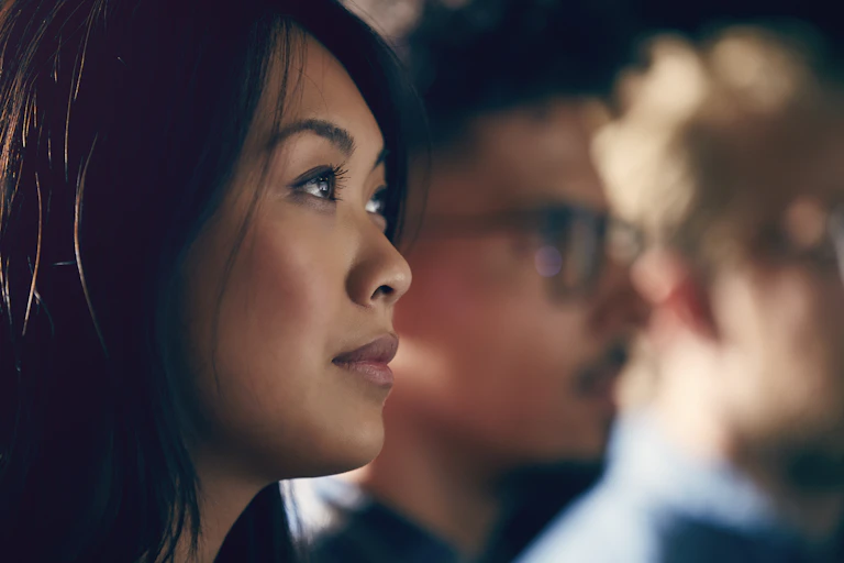 A young Asian American woman watches a presentation.