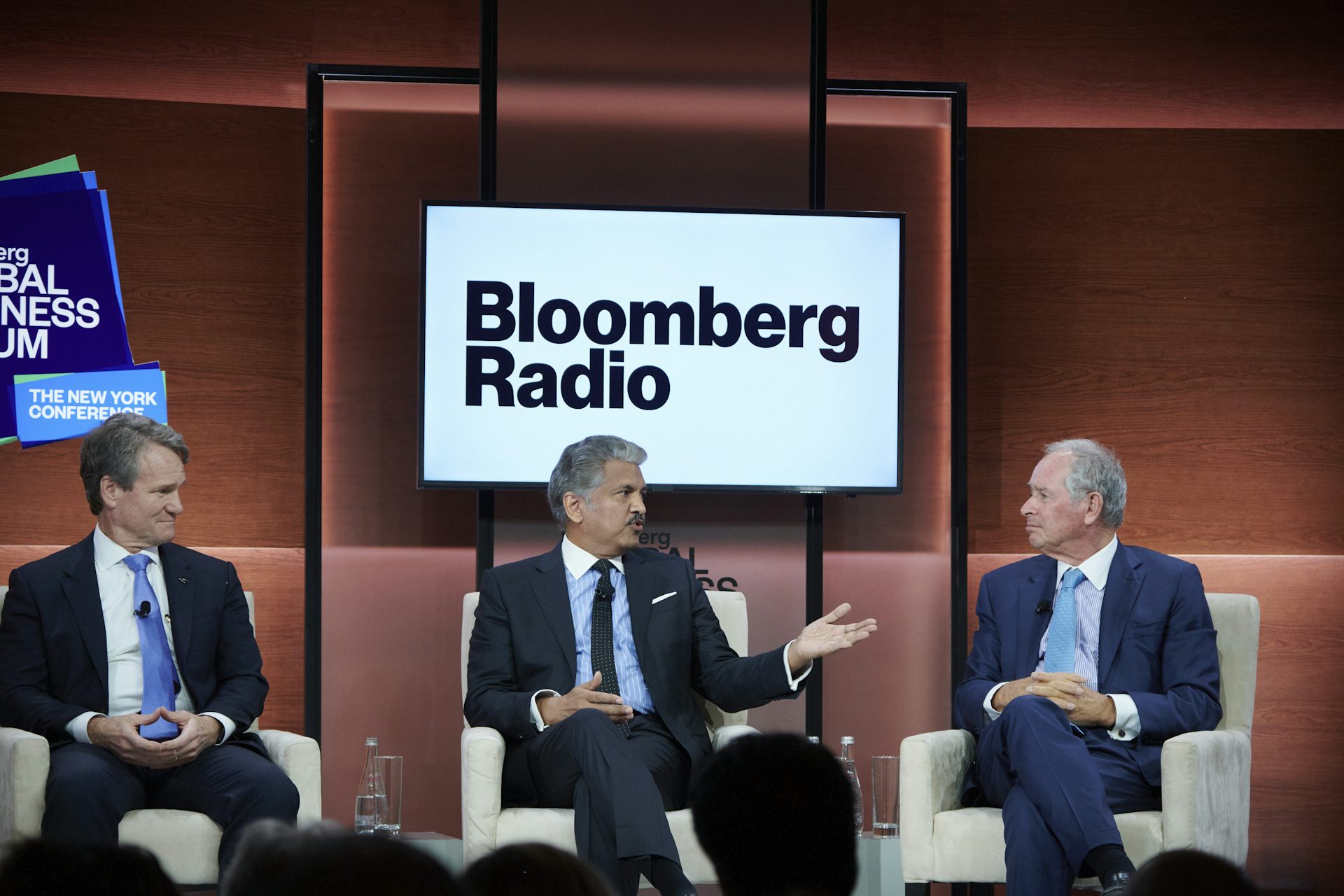Three CEOs sit on comfy chairs in front of a Bloomberg Radio sign on a screen.