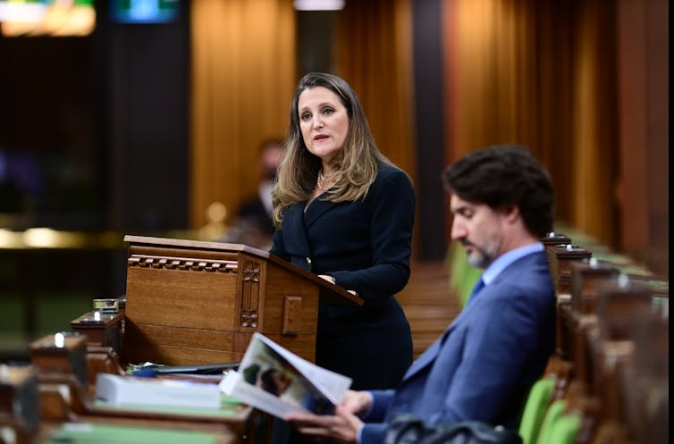 Freeland delivers the budget as Trudeau sits beside her reading the document.