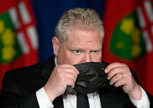 Premier Doug Ford raising a black face mask to his face