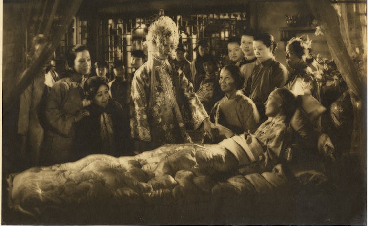 A bride stands by an ill woman in bed.