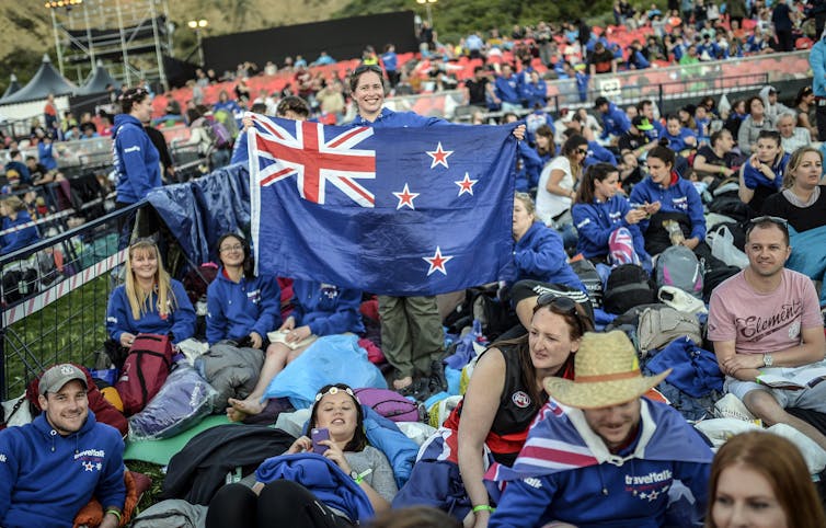 Woman holding the New Zealand flag with crowd of young people