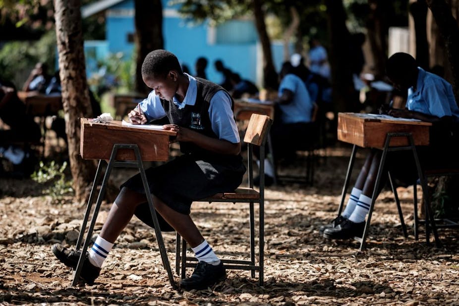 Students sitting on their chairs and desks taking a test outside.