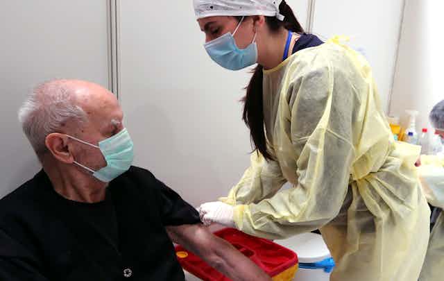 A nurse administering a dose of the AstraZeneca vaccine to a man