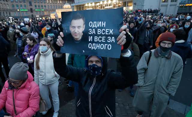 A protester in St Petersburg, Russia holds up a banner with a picture of dissident leader Alexei Navalny. In the background are thousands of other demonstrators.